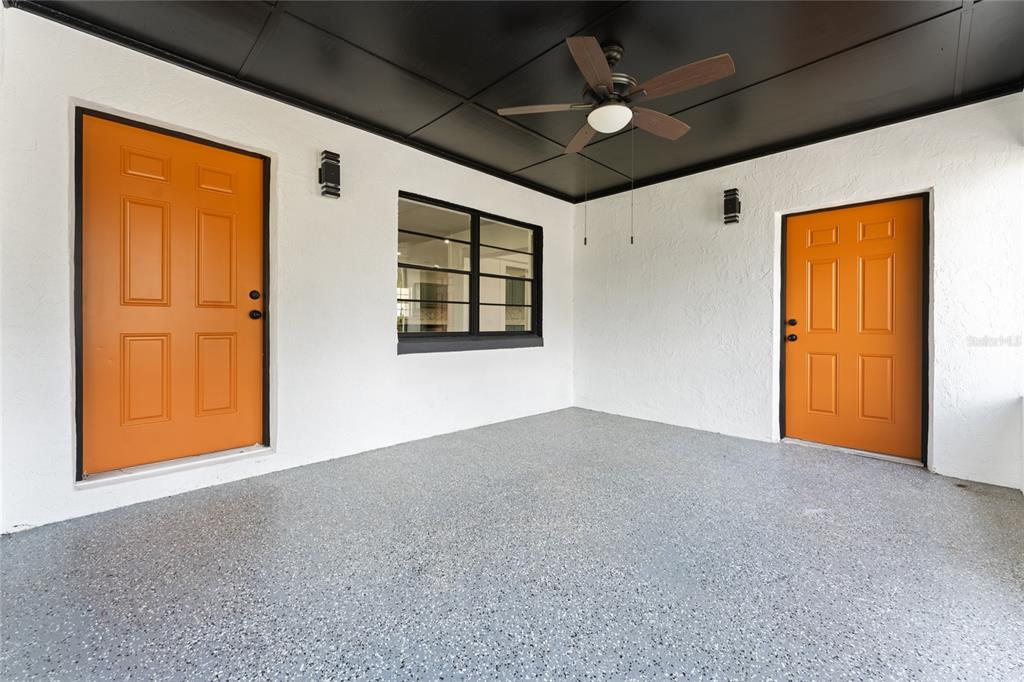 A covered patio features white walls, a black ceiling, two orange doors, and speckled flooring — 637 PASADENA AVENUE, LONGWOOD, FL