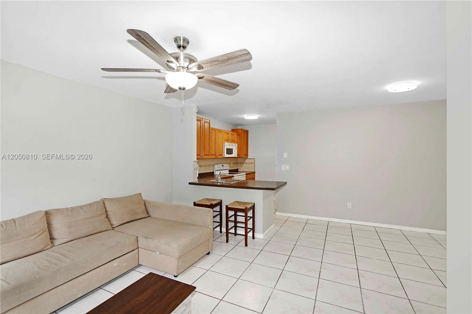 A living room with a sectional sofa and ceiling fan opens to a kitchen area — 2530 W 67th Pl # 29, Hialeah FL 33016, HIALEAH, FL