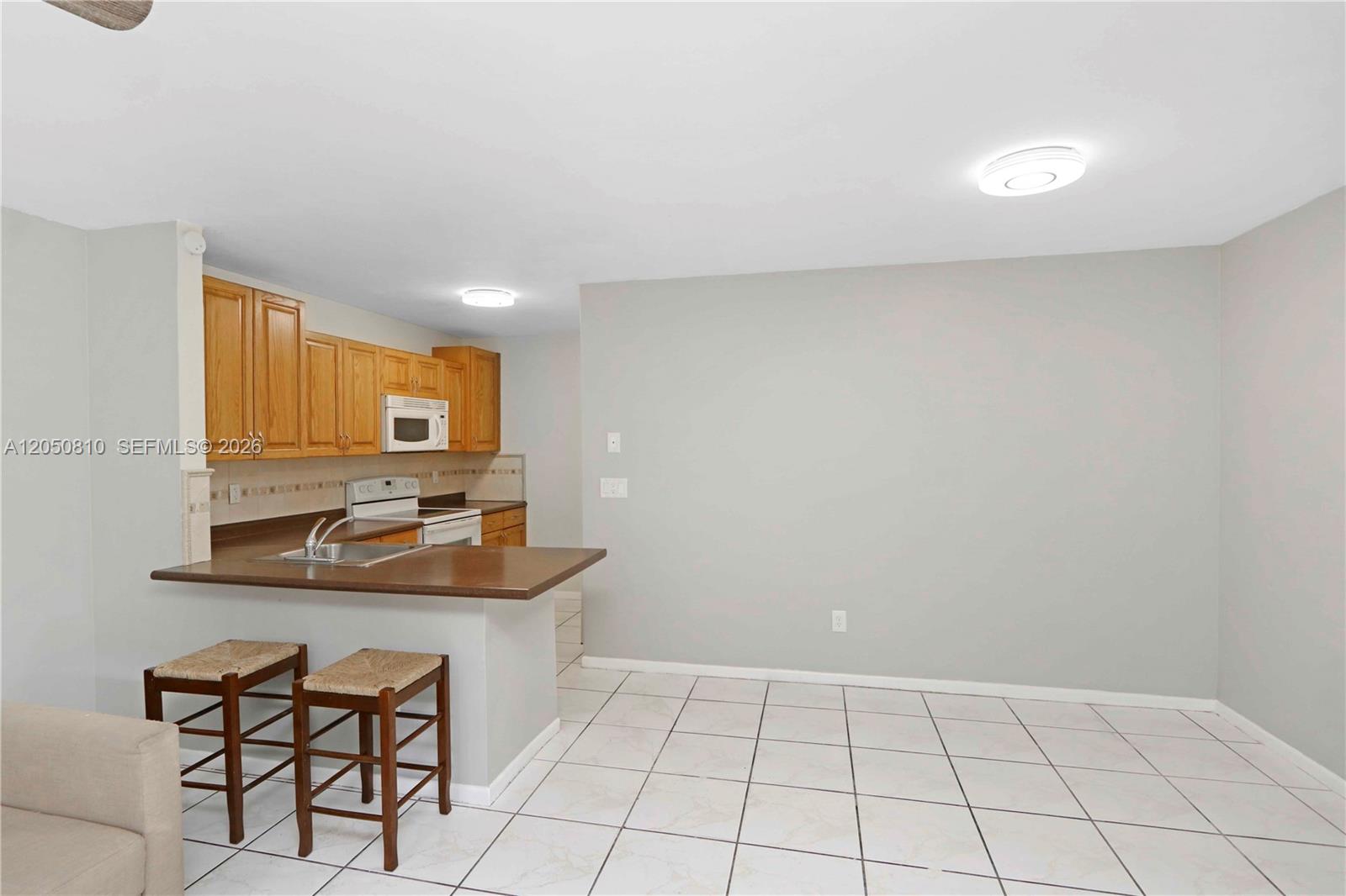 A kitchen with wooden cabinets and a breakfast bar overlooks a tiled dining area — 2530 W 67th Pl # 29, Hialeah FL 33016, HIALEAH, FL