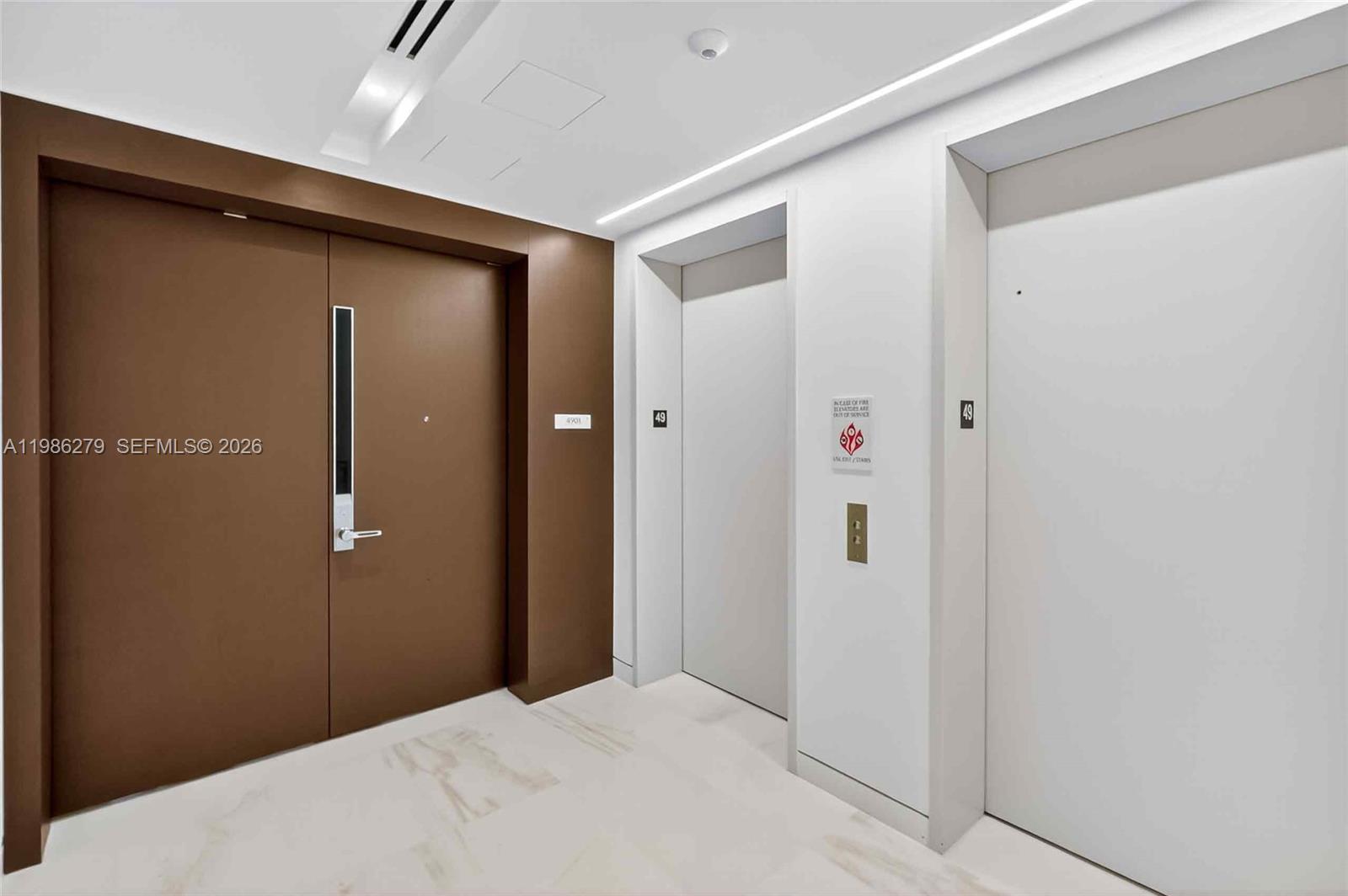 A modern hallway features a brown door, two white elevator doors, and marble flooring — 300 Biscayne Blvd Way # 4901E, Miami FL 33131, MIAMI, FL
