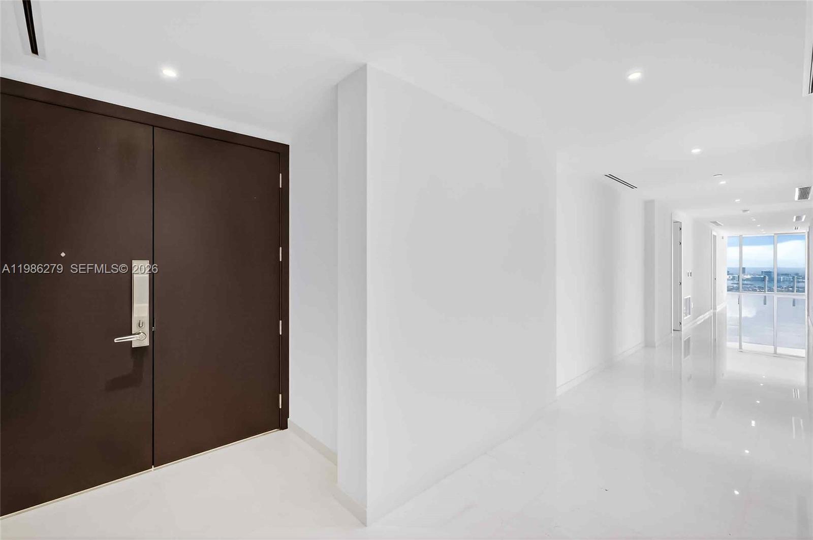 A minimalist entryway features a dark double door, white walls, and polished white flooring — 300 Biscayne Blvd Way # 4901E, Miami FL 33131, MIAMI, FL