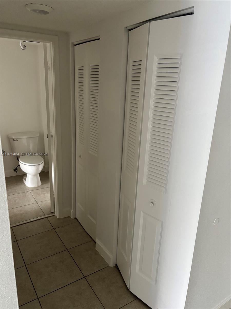 A tiled hallway leads to a bathroom with a toilet and two louvered closet doors — 7900 Camino Cir # 308, Miami FL 33143, MIAMI, FL