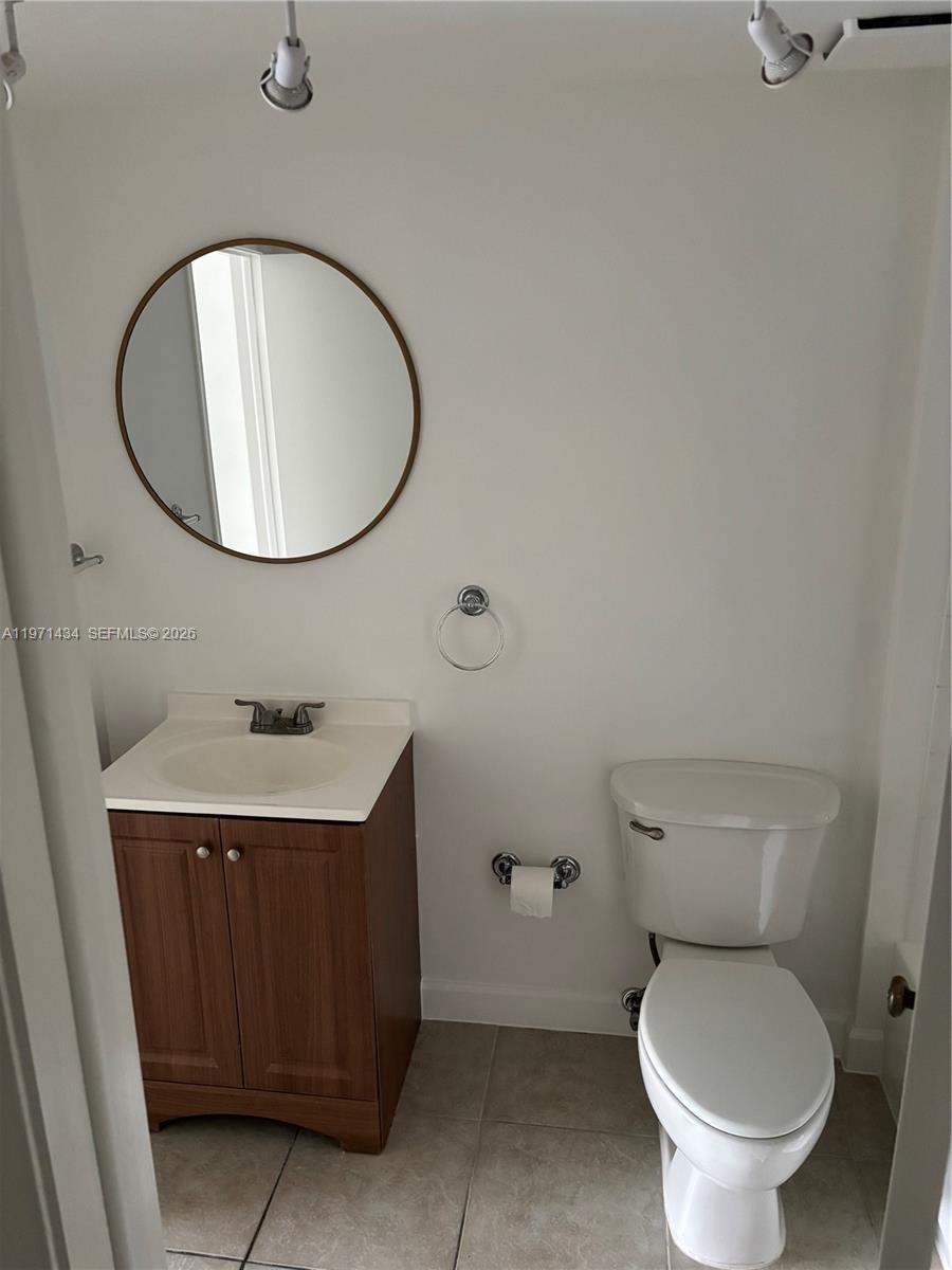 A bathroom features a wood vanity, a round mirror, and a white toilet — 7900 Camino Cir # 308, Miami FL 33143, MIAMI, FL