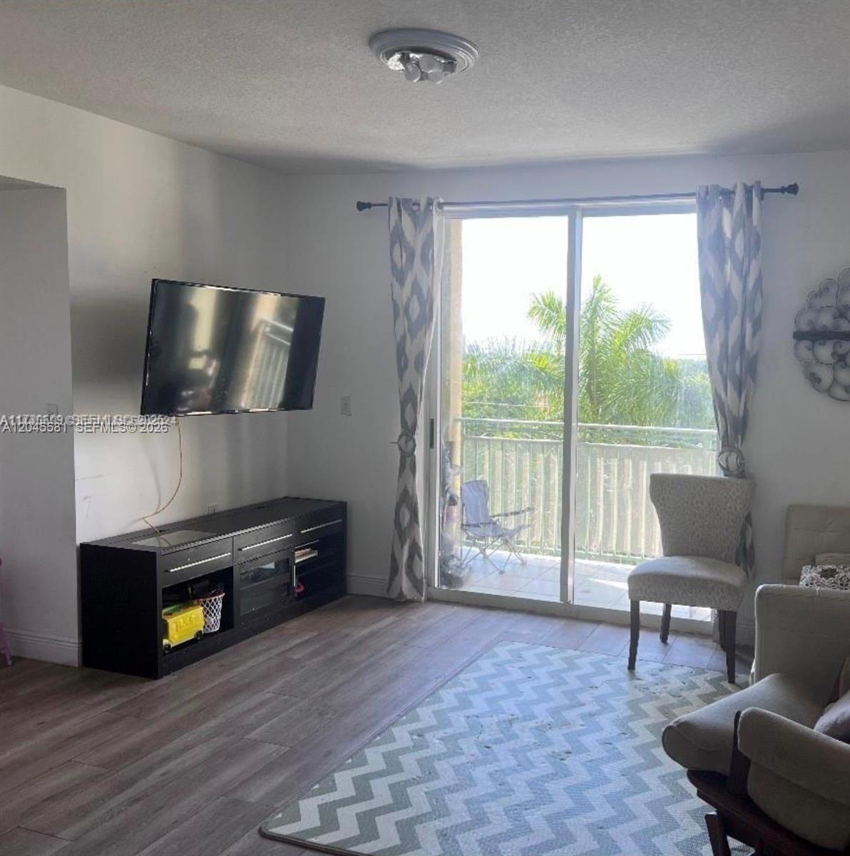 A living room features a wall-mounted television, a black media console, and a sliding glass door — 3500 Coral Way # 513, Miami FL 33145, MIAMI, FL