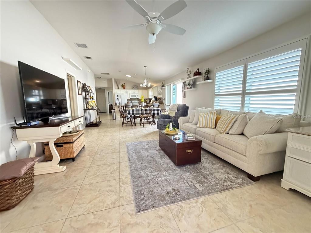 This open-concept living and dining area features tile flooring, a ceiling fan, and neutral furniture — 1963 LADYFISH AVENUE, THE VILLAGES, FL