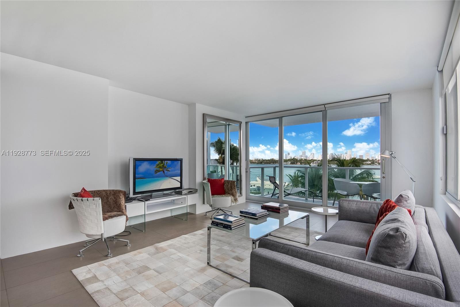A modern living room features a gray sofa, glass coffee table, and floor-to-ceiling balcony windows — 1000 West Ave # 311, Miami Beach FL 33139, MIAMI BEACH, FL