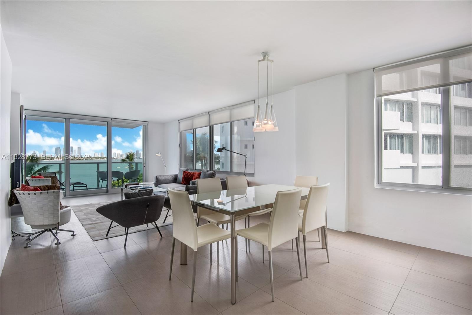 A modern dining and living area features a glass table, neutral furniture, and waterfront views — 1000 West Ave # 311, Miami Beach FL 33139, MIAMI BEACH, FL
