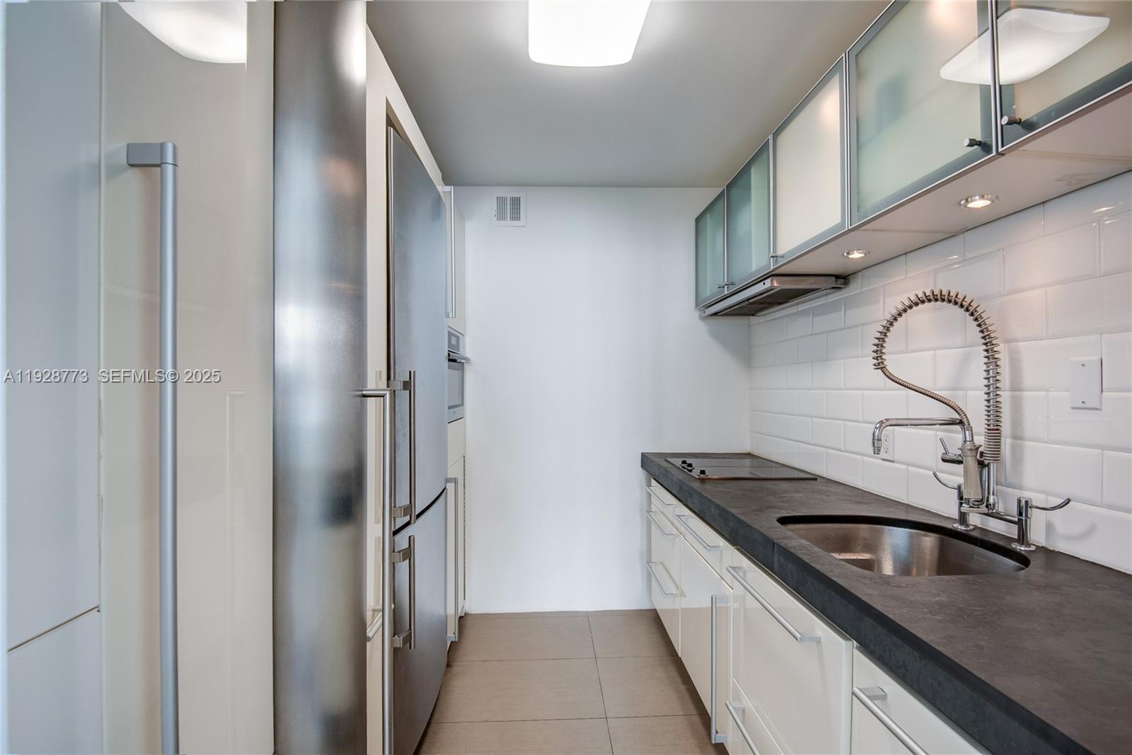 A galley kitchen features white cabinets, dark countertops, stainless steel appliances, and subway tile backsplash — 1000 West Ave # 311, Miami Beach FL 33139, MIAMI BEACH, FL