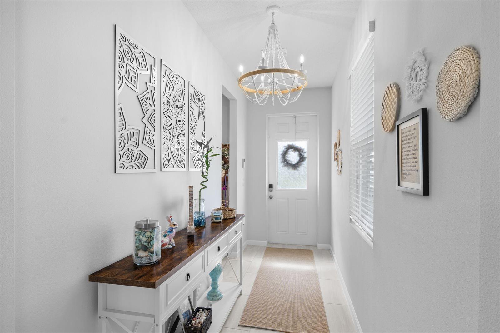 A bright entryway features a white console table, a beaded chandelier, and wall art — 1254 Canfield Circle SE, Palm Bay FL 32909, PALM BAY, FL