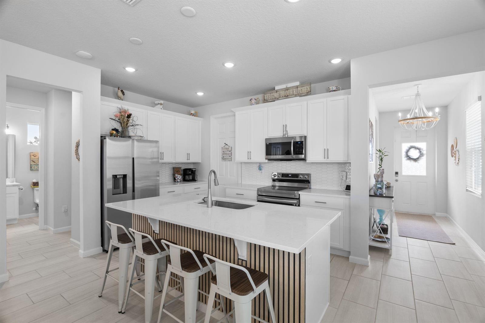 A modern kitchen features white cabinetry, a quartz-topped island with wood slats, and stainless appliances — 1254 Canfield Circle SE, Palm Bay FL 32909, PALM BAY, FL