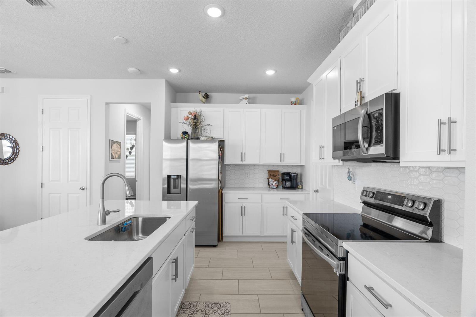 A modern kitchen features white cabinets, stainless steel appliances, a large island, and tile flooring — 1254 Canfield Circle SE, Palm Bay FL 32909, PALM BAY, FL