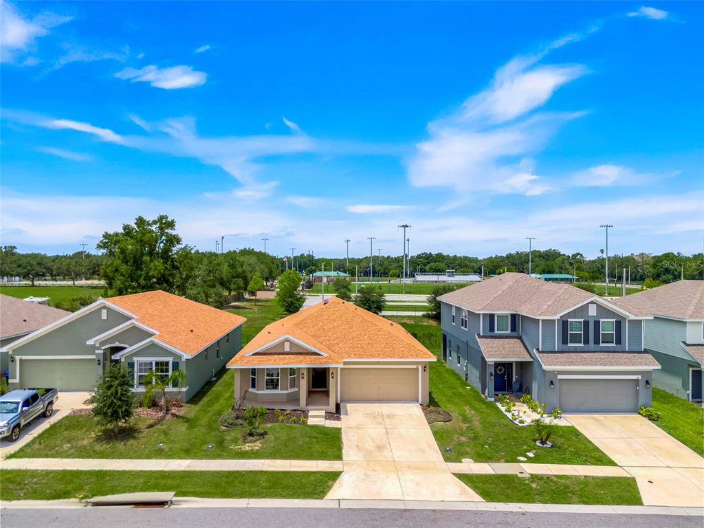 An aerial view shows three suburban houses with driveways and lawns facing a sports field — 140 KRENSON BAY LOOP, WINTER HAVEN, FL