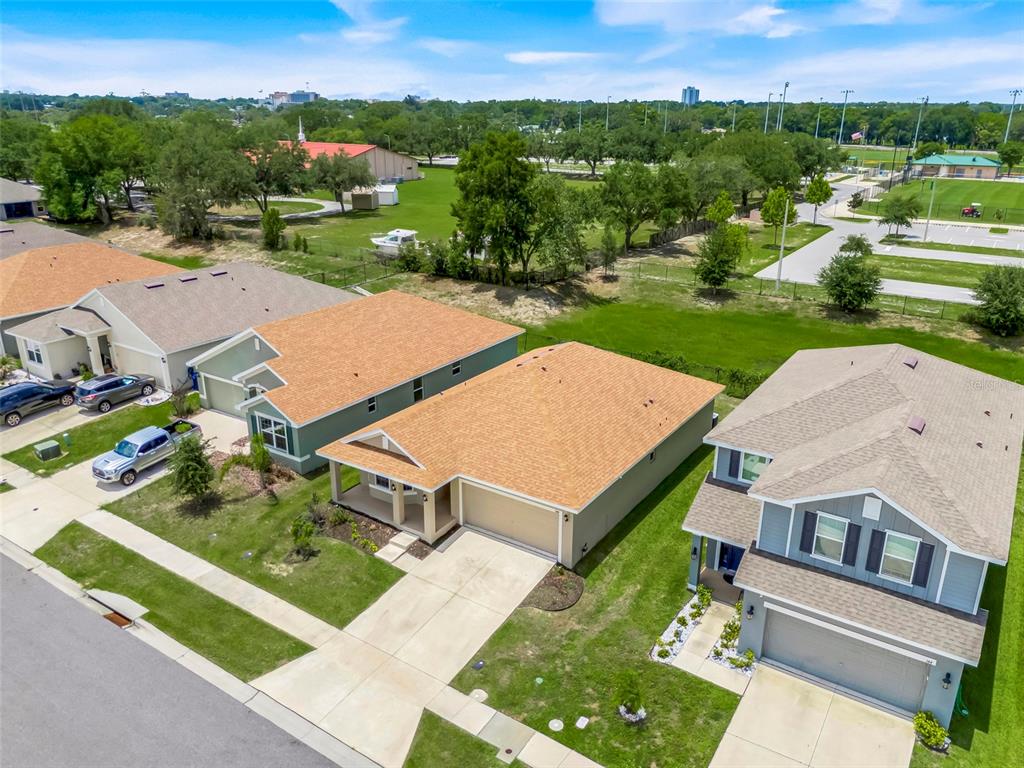 An aerial view shows three suburban houses with tan roofs and driveways near a grassy field — 140 KRENSON BAY LOOP, WINTER HAVEN, FL