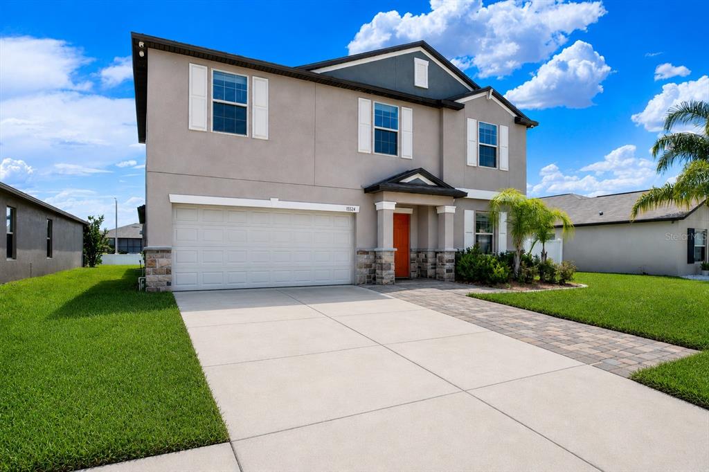 A two-story suburban house with a beige stucco exterior, a red front door, and a lawn — 13524 WILD GINGER STREET, RIVERVIEW, FL