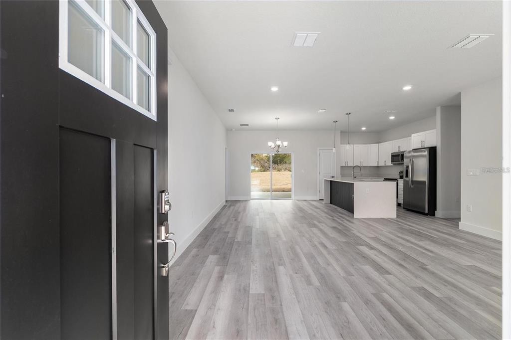 An open-concept living area with light wood-look flooring leads to a kitchen and sliding doors — 13633 SW 82ND AVENUE, OCALA, FL