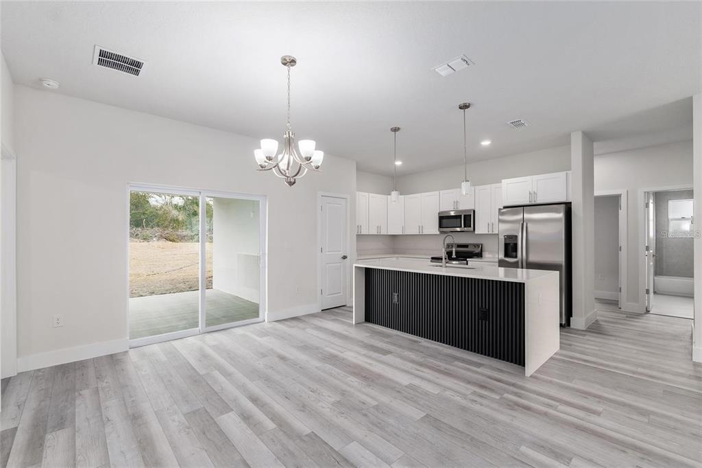 A modern kitchen and dining area with white cabinets, a black-paneled island, and sliding doors — 13633 SW 82ND AVENUE, OCALA, FL