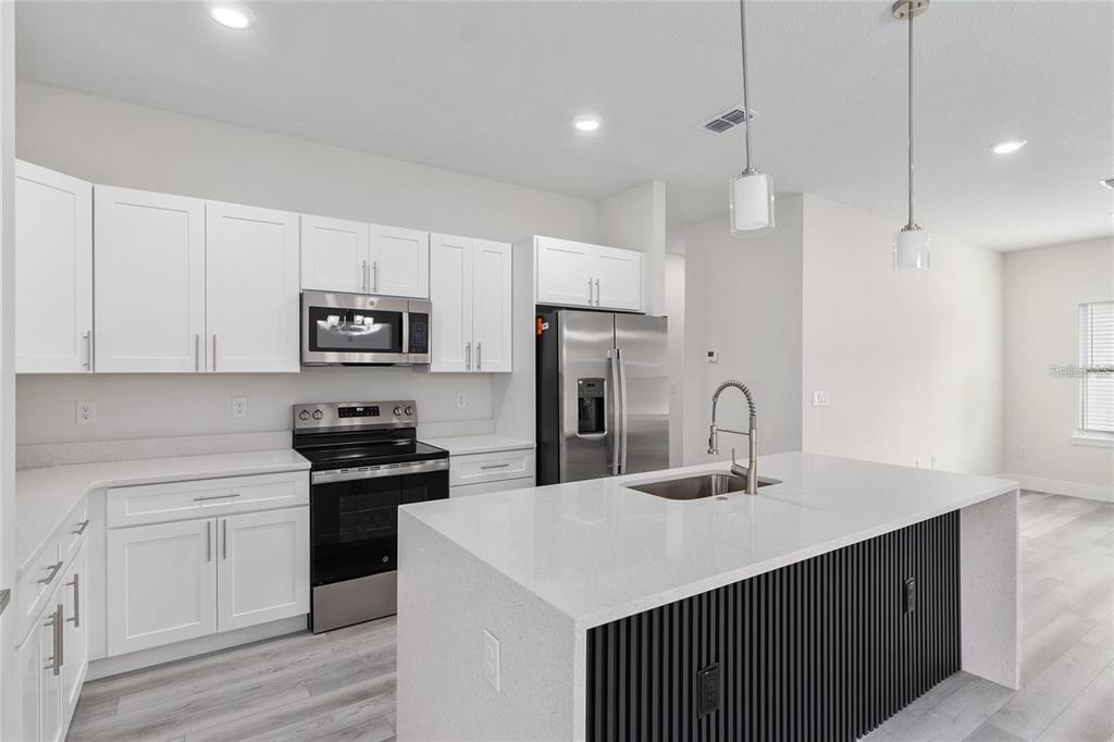 A modern kitchen features white cabinets, stainless steel appliances, and a large quartz-topped island — 13633 SW 82ND AVENUE, OCALA, FL
