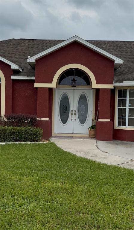The exterior of a house features a red stucco facade with a double-door arched entryway — 4470 GONDOLIER ROAD, SPRING HILL, FL