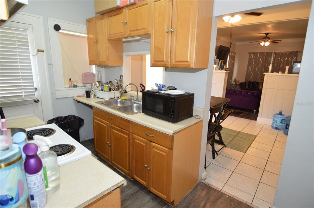 A kitchen with wood cabinets, a double sink, and a microwave overlooks a living area — 1244 20TH AVENUE S, ST PETERSBURG, FL