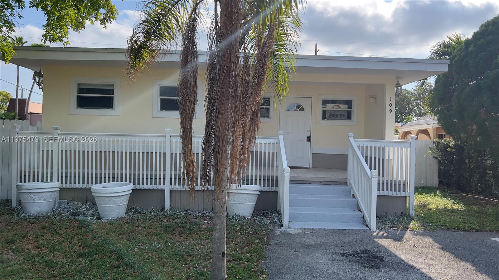 A pale yellow house features a white front porch, stairs, and a palm tree — 109 SW 1st Ave, Hallandale Beach FL 33009, HALLANDALE BEACH, FL