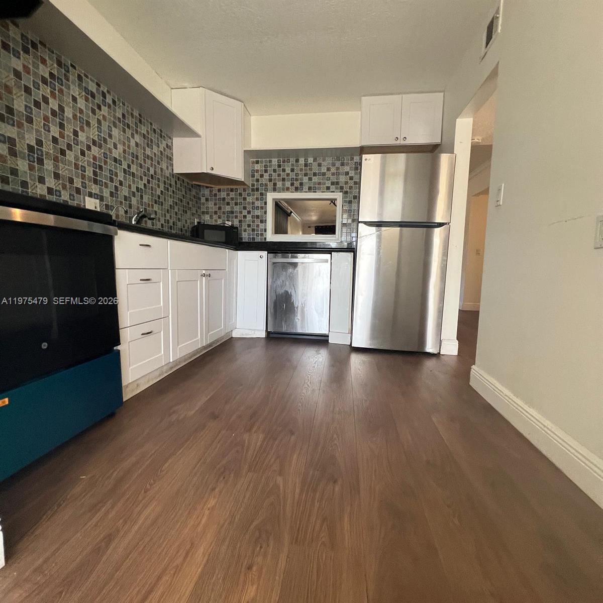 A kitchen features white cabinets, stainless steel appliances, and a multi-colored mosaic tile backsplash — 109 SW 1st Ave, Hallandale Beach FL 33009, HALLANDALE BEACH, FL