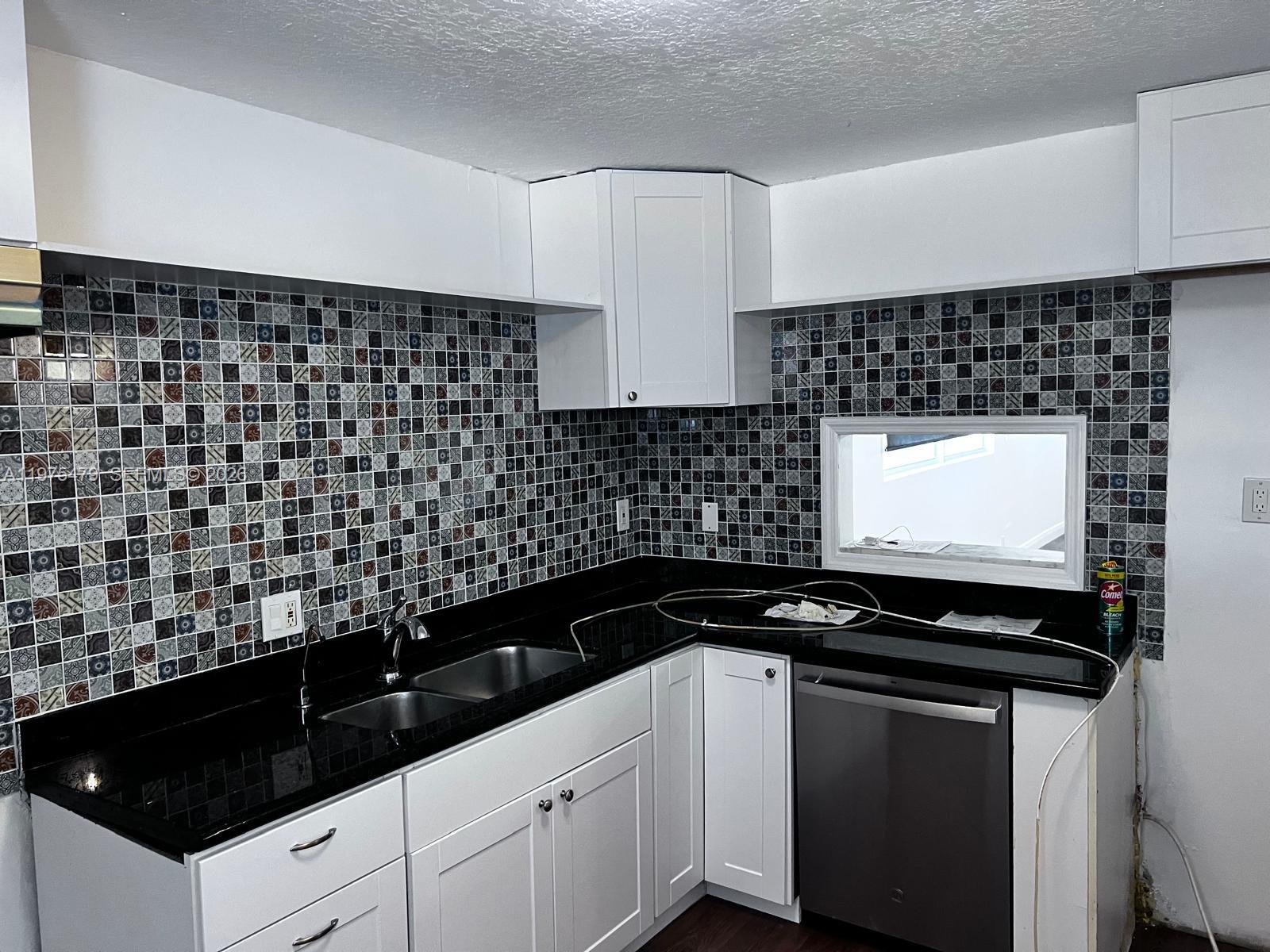 A kitchen features white cabinets, black countertops, and a patterned mosaic tile backsplash — 109 SW 1st Ave, Hallandale Beach FL 33009, HALLANDALE BEACH, FL
