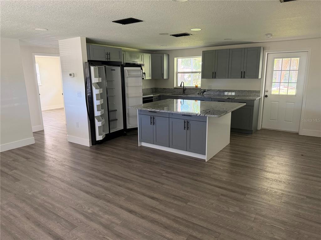 A kitchen with gray cabinets, a granite-topped island, and light wood-look flooring — 6845 CAROB DRIVE, NEW PORT RICHEY, FL