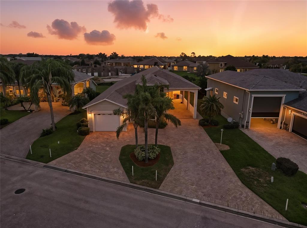 An aerial view shows a suburban house with a paved driveway and palm trees at sunset — 529 MEANDERING WAY, POLK CITY, FL