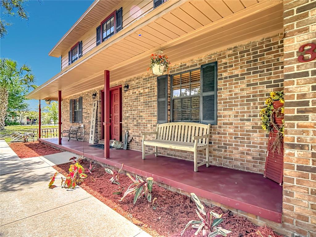 A brick house features a covered front porch with a wooden bench and red flooring — 3465 JAMIE STREET, MULBERRY, FL