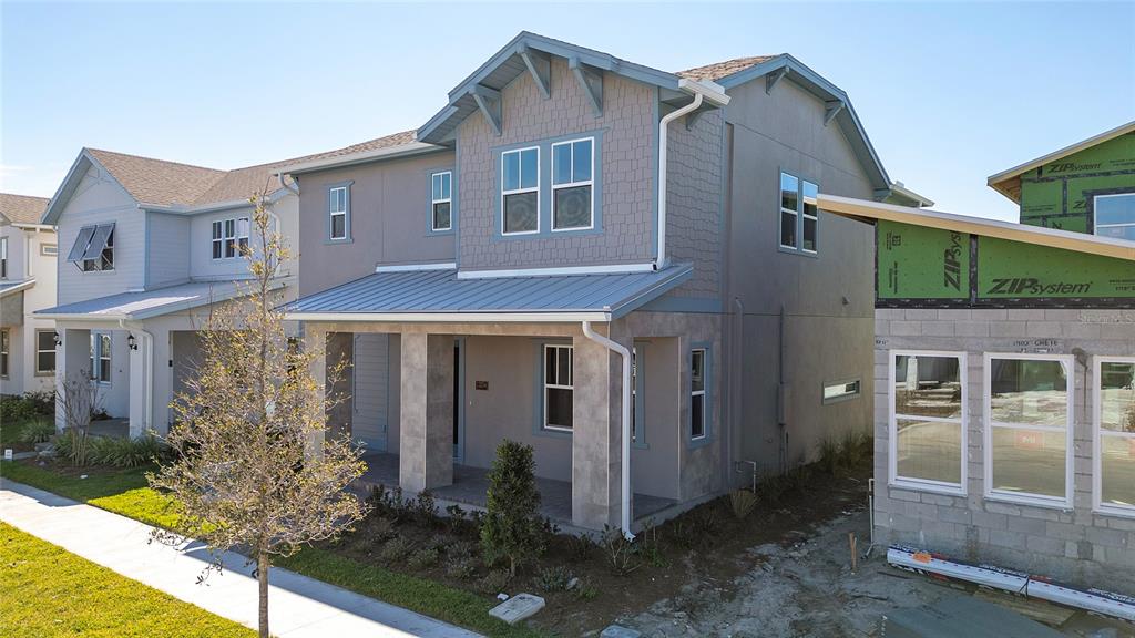 A two-story house with a metal-roofed porch and gray siding stands next to a construction site — 13254 MCMILLAN DRIVE, ORLANDO, FL