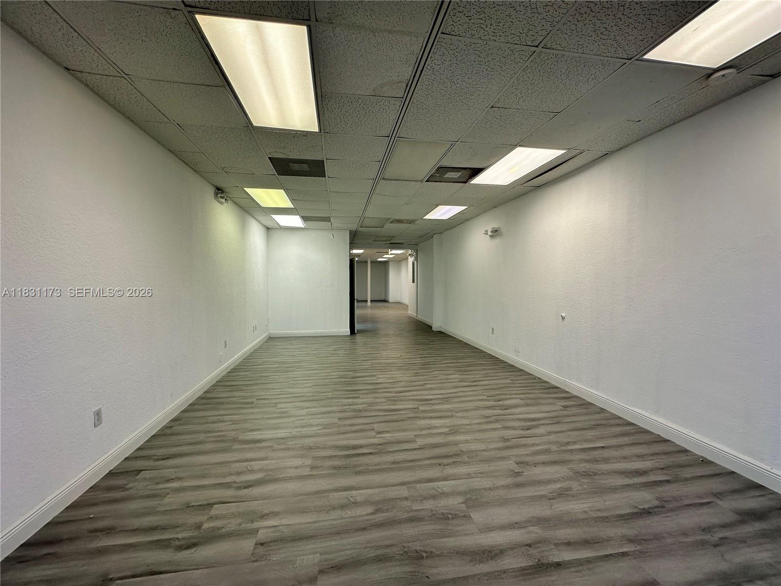 An empty commercial space features white walls, a drop ceiling with recessed lighting, and wood-look flooring — 2922 N State Road 7 # 2916, Margate FL 33063, MARGATE, FL