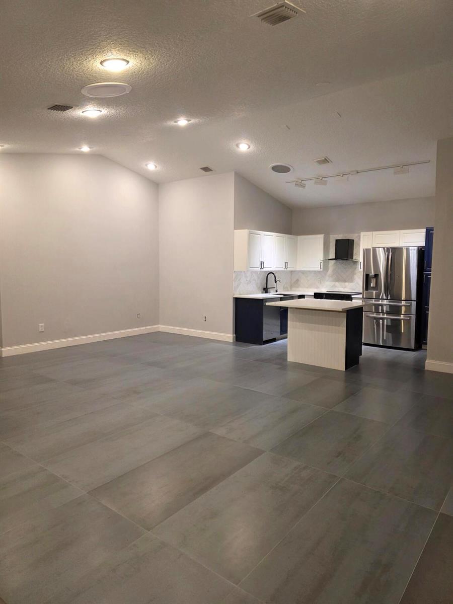 A modern open-concept kitchen features dark lower cabinets, white upper cabinets, and large gray tiles — 5852 Eagle Cay Terrace, Coconut Creek FL 33073, COCONUT CREEK, FL