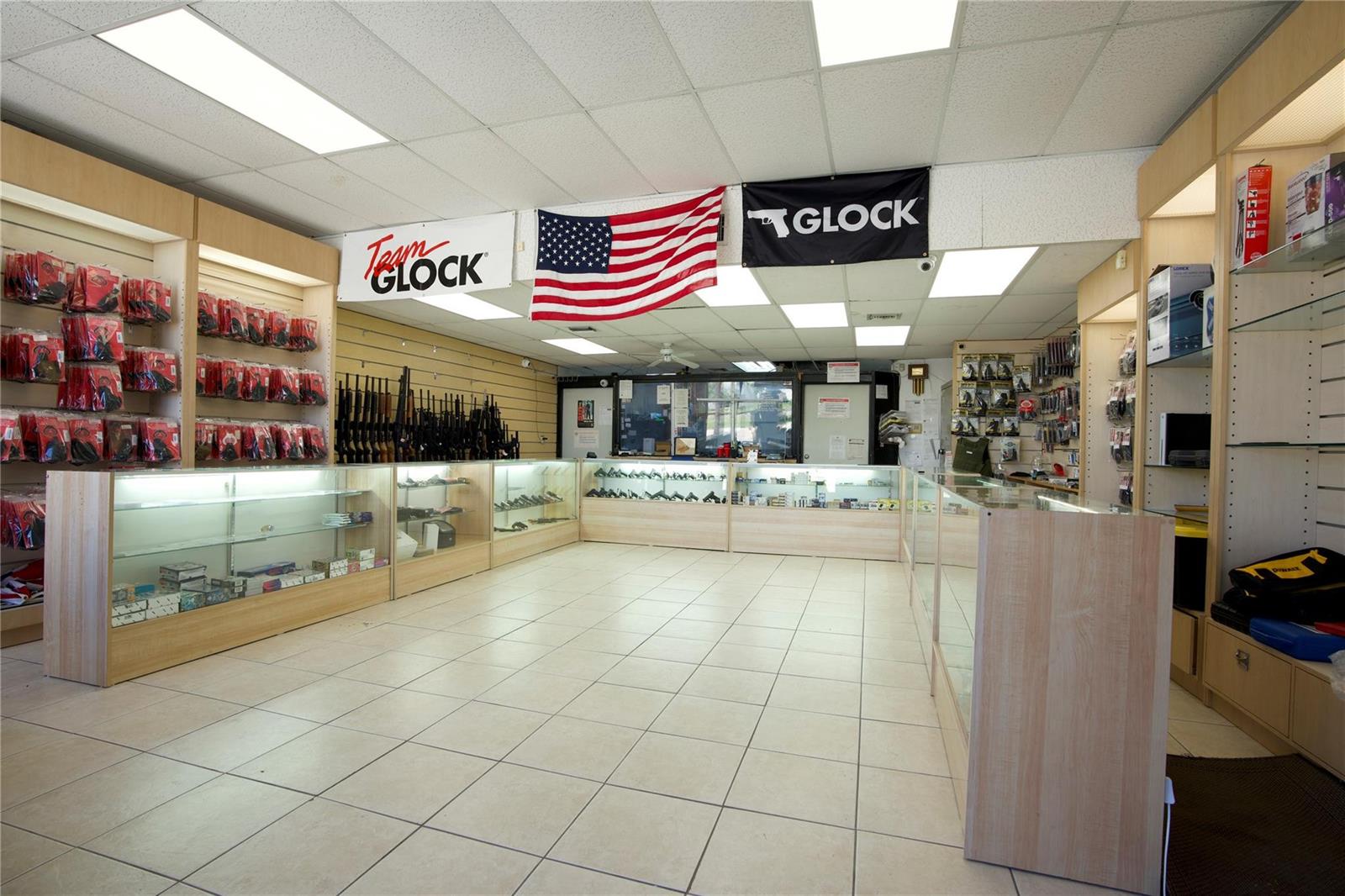 A retail gun store interior features glass display cases, wall-mounted firearms, and Glock signage — 4581 N Dixie Highway, Deerfield Beach FL 33064, DEERFIELD BEACH, FL