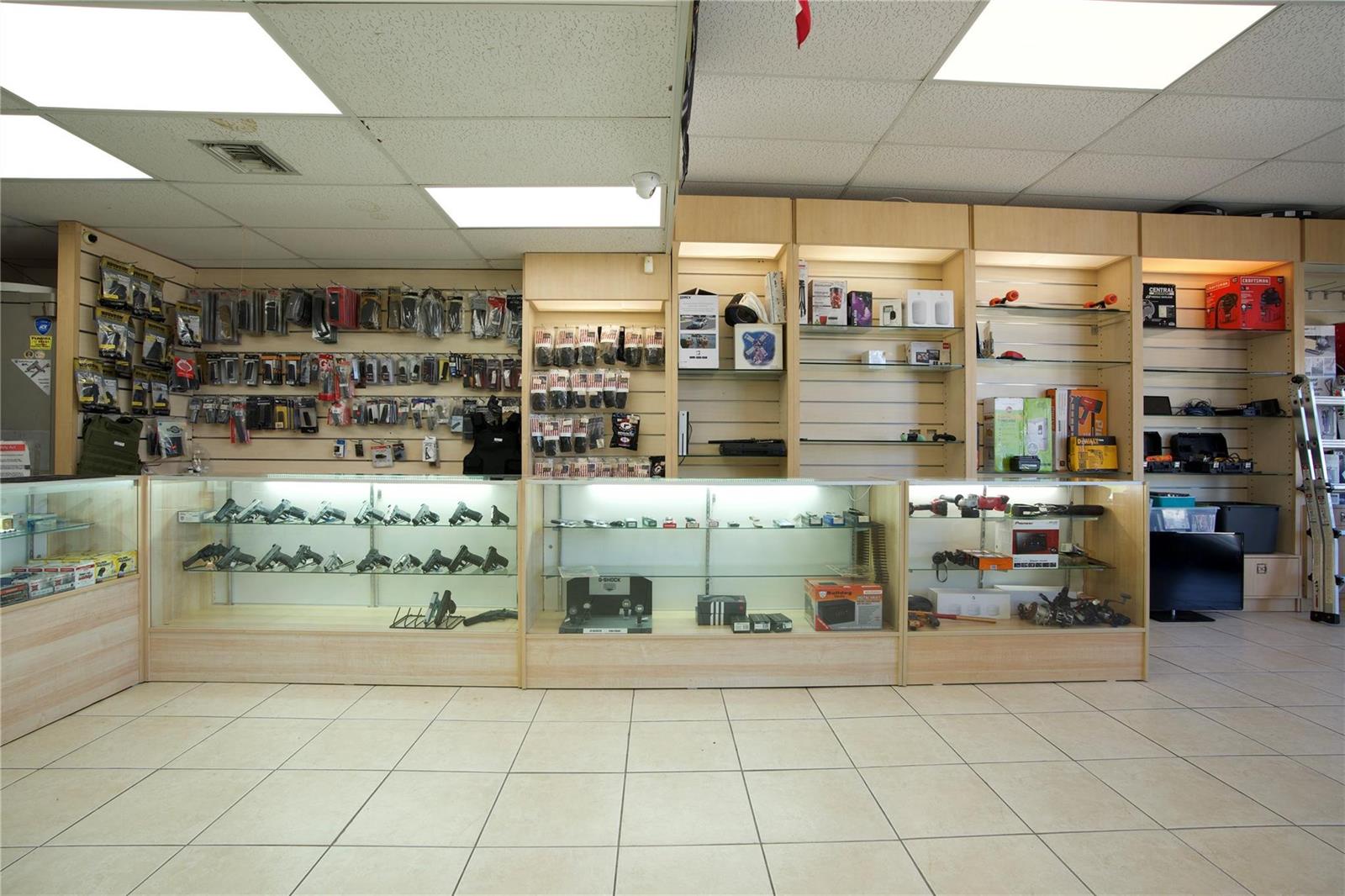 A retail store interior features glass display cases filled with firearms and wall-mounted merchandise shelves — 4581 N Dixie Highway, Deerfield Beach FL 33064, DEERFIELD BEACH, FL