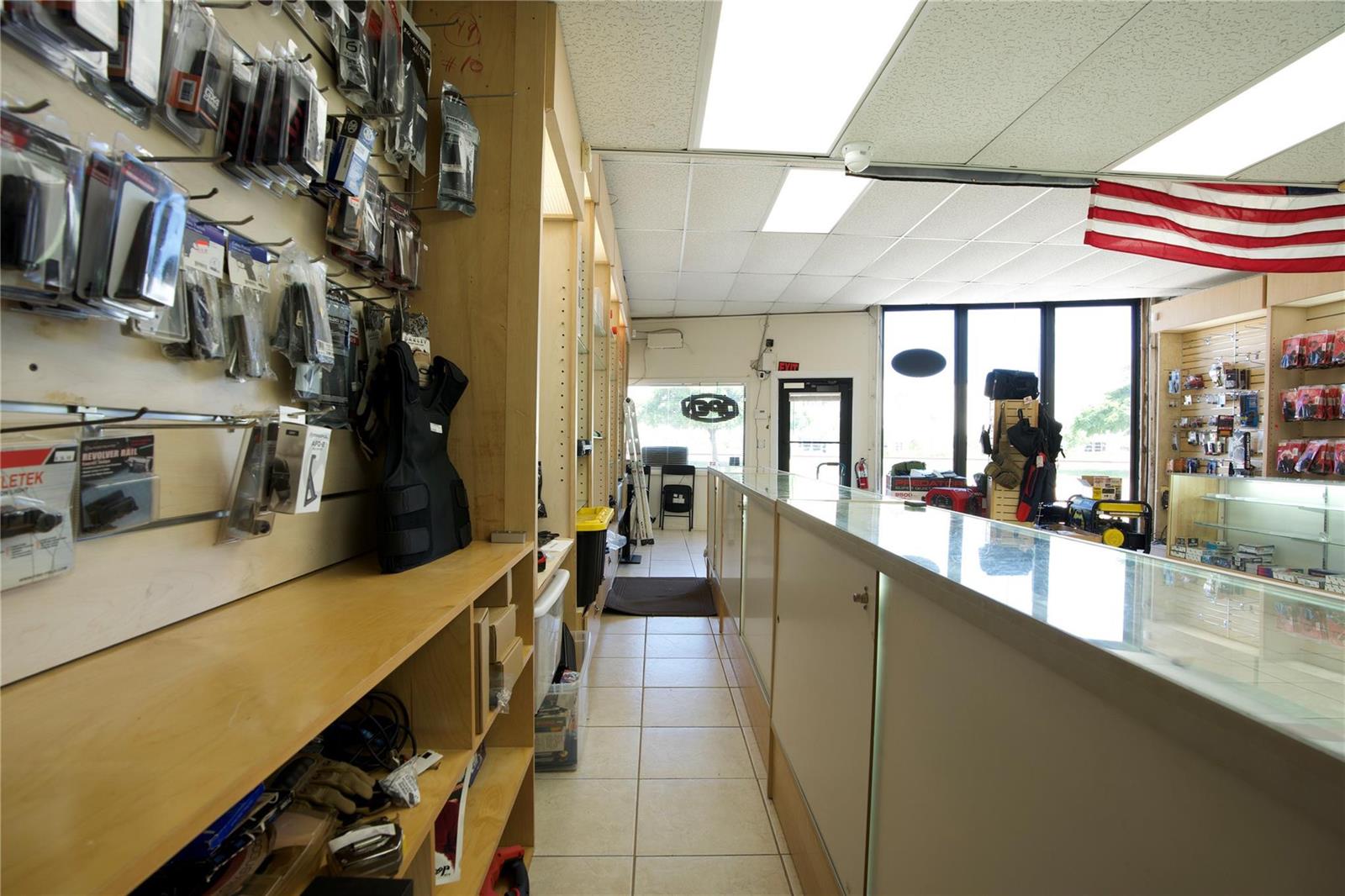 A retail store interior features a long glass display counter, wall-mounted merchandise, and tile flooring — 4581 N Dixie Highway, Deerfield Beach FL 33064, DEERFIELD BEACH, FL