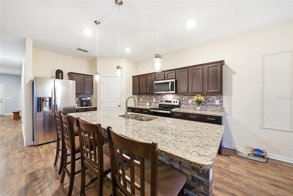 A kitchen features dark wood cabinets, granite countertops, a large island, and stainless steel appliances — 1151 LYCASTE DRIVE, DAVENPORT, FL