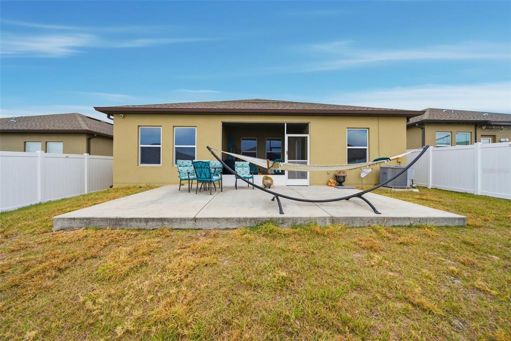 A tan house exterior features a concrete patio, a hammock, and a white privacy fence — 1151 LYCASTE DRIVE, DAVENPORT, FL