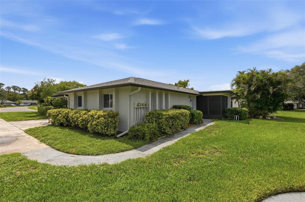 A single-story house with a beige exterior, a screened-in porch, and a landscaped front yard — 1339 QUEEN ANNE DRIVE UNIT C, PALM HARBOR, FL