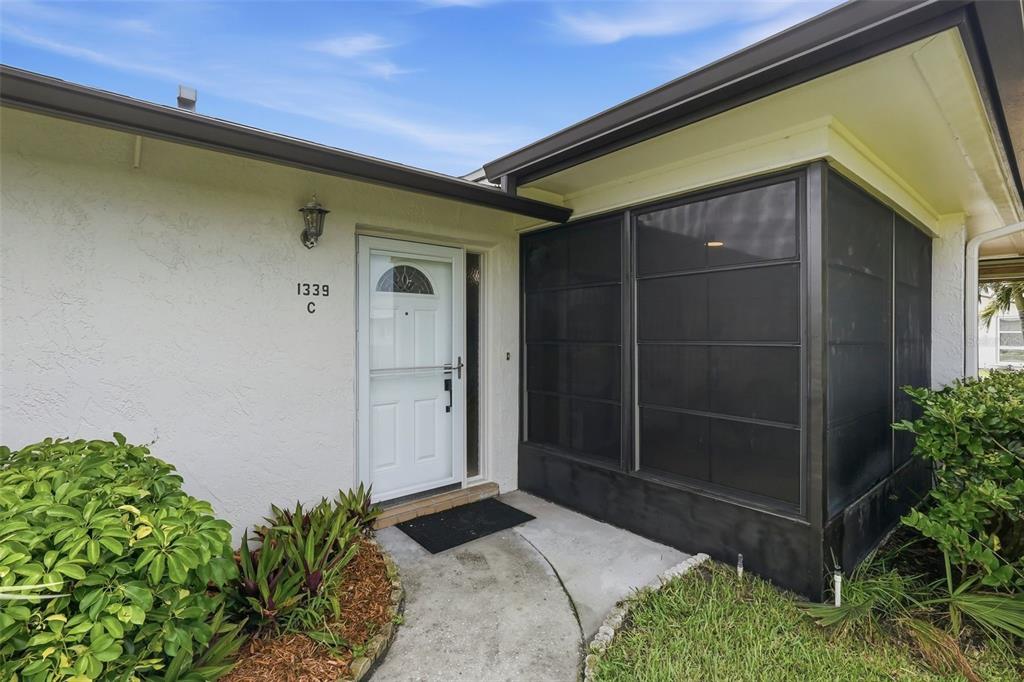 The exterior view shows a white front door with a screened-in porch and landscaping — 1339 QUEEN ANNE DRIVE UNIT C, PALM HARBOR, FL
