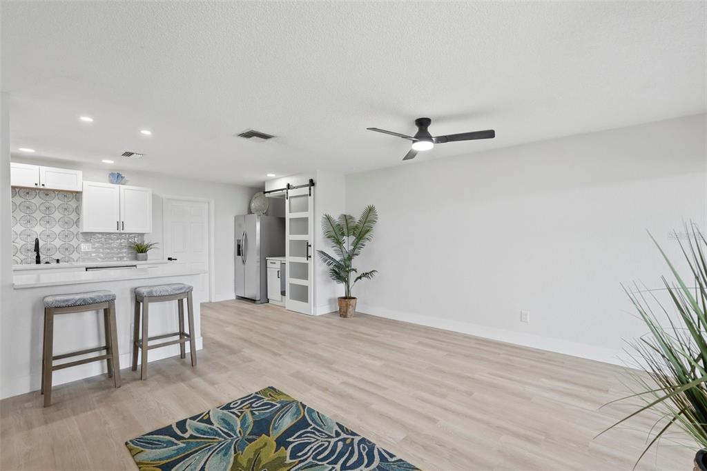 A bright, open-concept kitchen and living area features light wood flooring and a sliding barn door — 1339 QUEEN ANNE DRIVE UNIT C, PALM HARBOR, FL