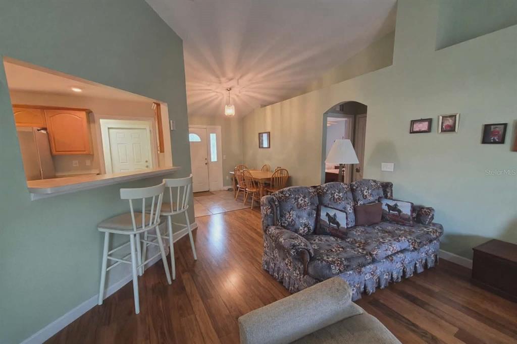 A living room with wood flooring, a floral sofa, and a breakfast bar overlooking the kitchen — 14396 SW 19TH PLACE, OCALA, FL