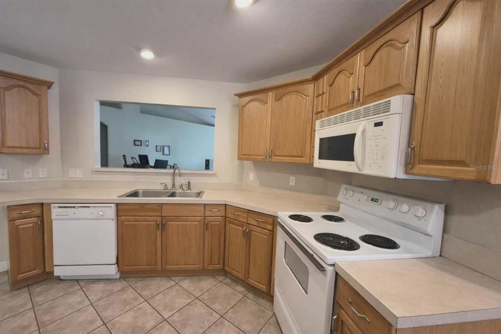 A kitchen features oak cabinets, white appliances, a double sink, and tiled flooring — 14396 SW 19TH PLACE, OCALA, FL