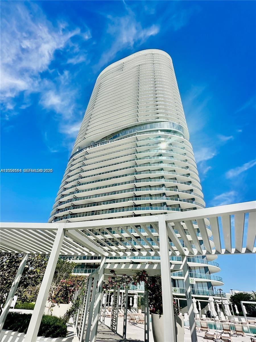 A low-angle view of a tall, modern white residential skyscraper with curved balconies — 500 ALTON RD # 1708, Miami Beach FL 33139, MIAMI BEACH, FL