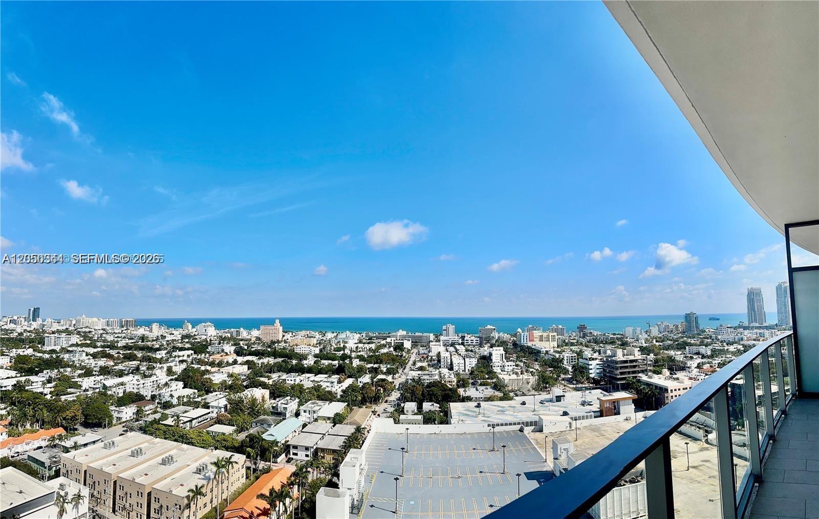 A high-angle view of a city skyline and ocean from a glass-railed balcony — 500 ALTON RD # 1708, Miami Beach FL 33139, MIAMI BEACH, FL