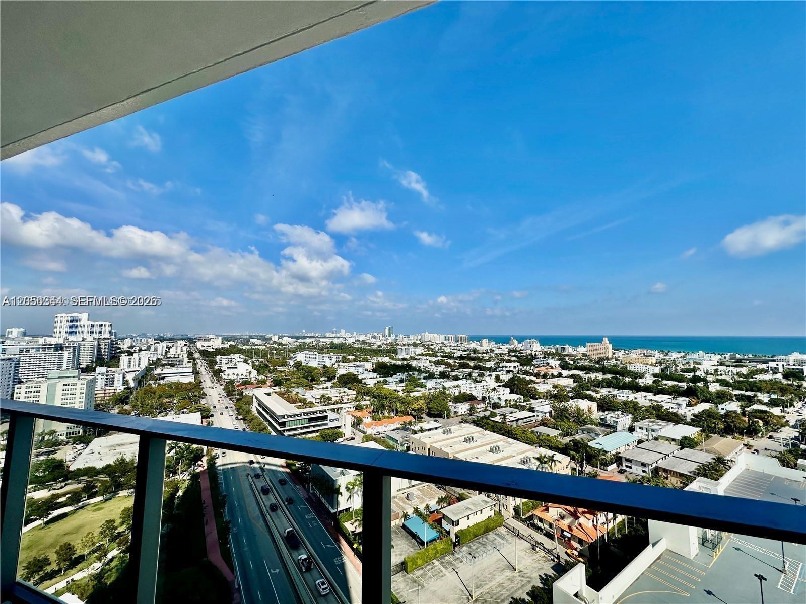 A high-angle view from a balcony overlooks a city street, residential buildings, and the ocean — 500 ALTON RD # 1708, Miami Beach FL 33139, MIAMI BEACH, FL