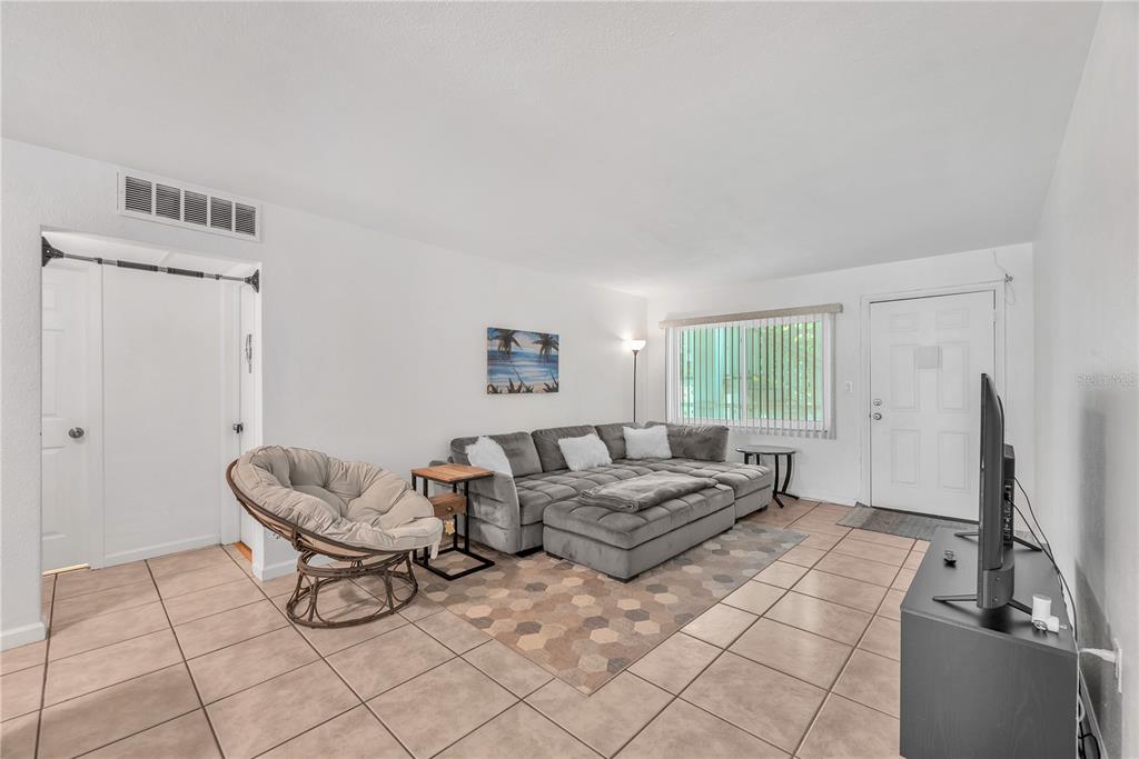 A living room features tile flooring, a gray sectional sofa, a papasan chair, and a door — 5155 9TH AVENUE N UNIT 211, ST PETERSBURG, FL