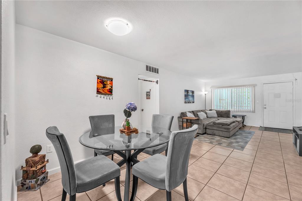 A dining area with a glass table and grey chairs opens into a living room — 5155 9TH AVENUE N UNIT 211, ST PETERSBURG, FL