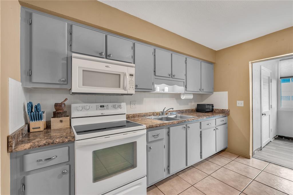 A kitchen features gray cabinets, white appliances, a tiled backsplash, and brown laminate countertops — 5155 9TH AVENUE N UNIT 211, ST PETERSBURG, FL