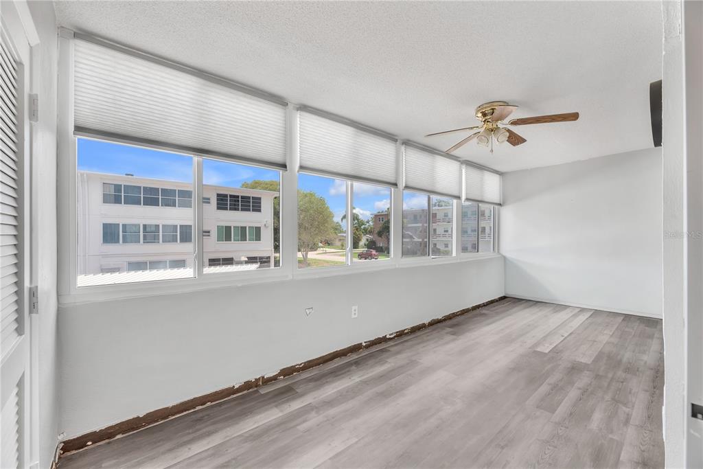 An enclosed sunroom features gray wood-look flooring, white walls, ceiling fan, and large windows — 5155 9TH AVENUE N UNIT 211, ST PETERSBURG, FL