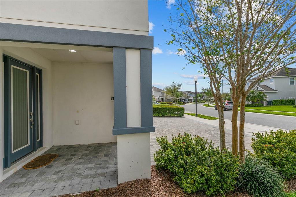 A covered entryway with a paved porch leads to a front door beside a suburban street — 7483 MARKER AVENUE, KISSIMMEE, FL